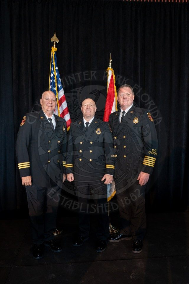 Three official firemen standing next to each other standing in front of United States of America flag and Florida flag.
