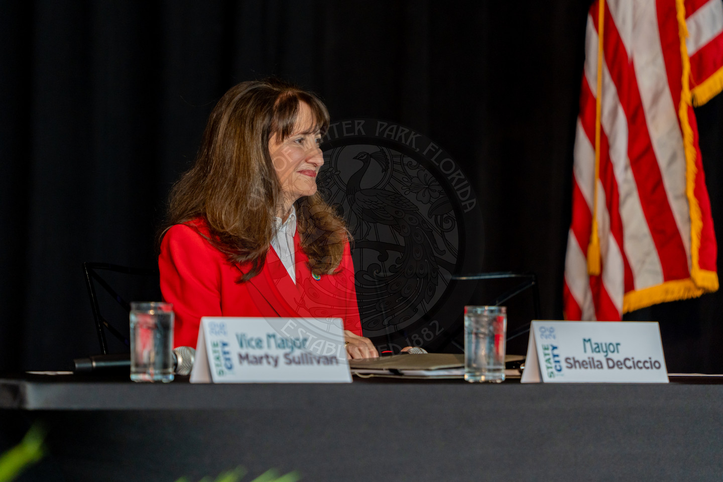 A woman sitting behind a table with a name card in front of her stating "Mayor Sheila DeCiccio"