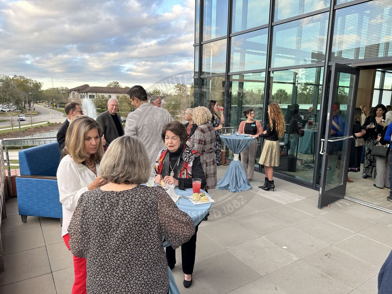 people mingling with each other talking and laughing out on the terrace with high top tables