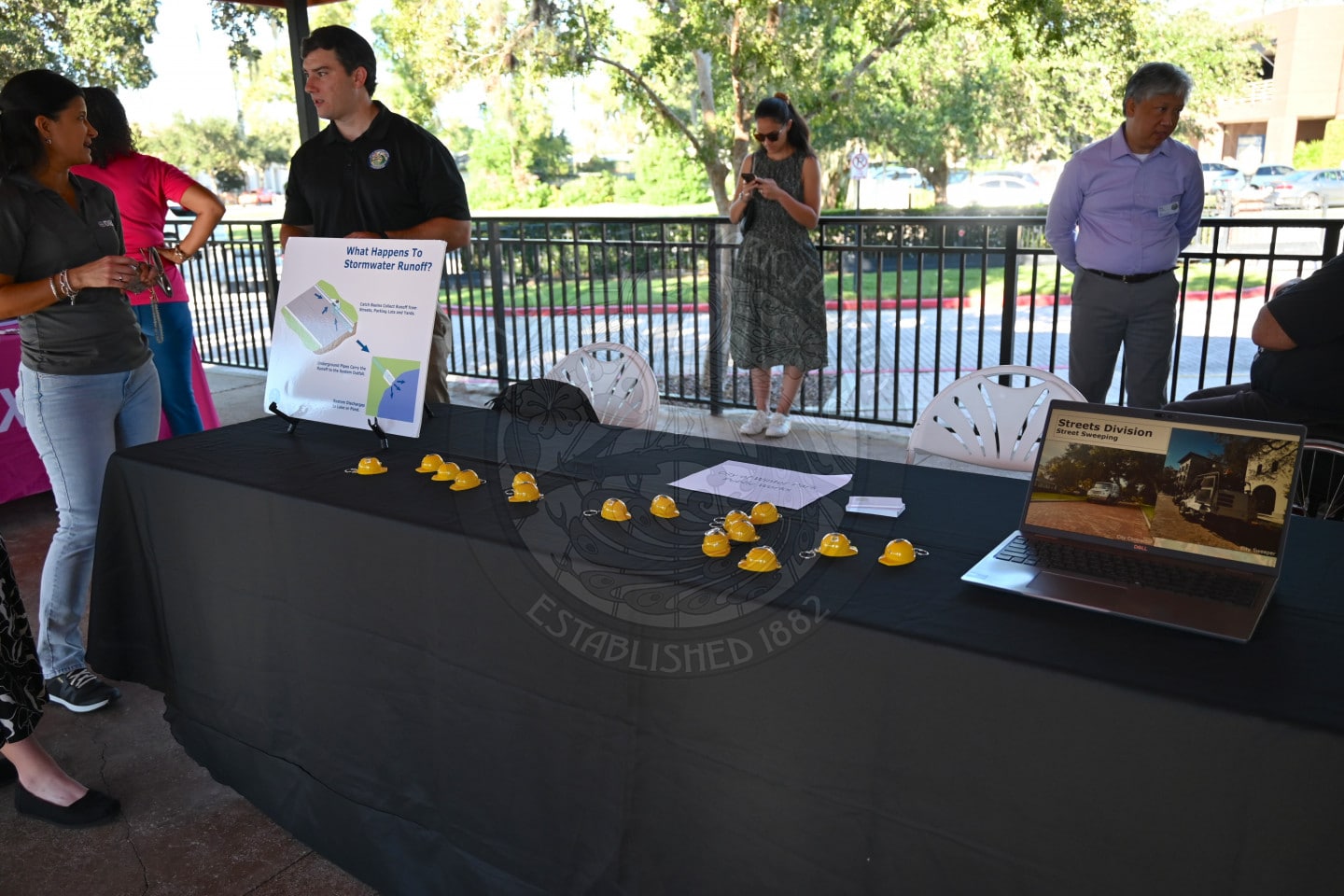 A man at a table discusses stormwater runoff with a visitor, with small yellow hard hat models displayed on the table.