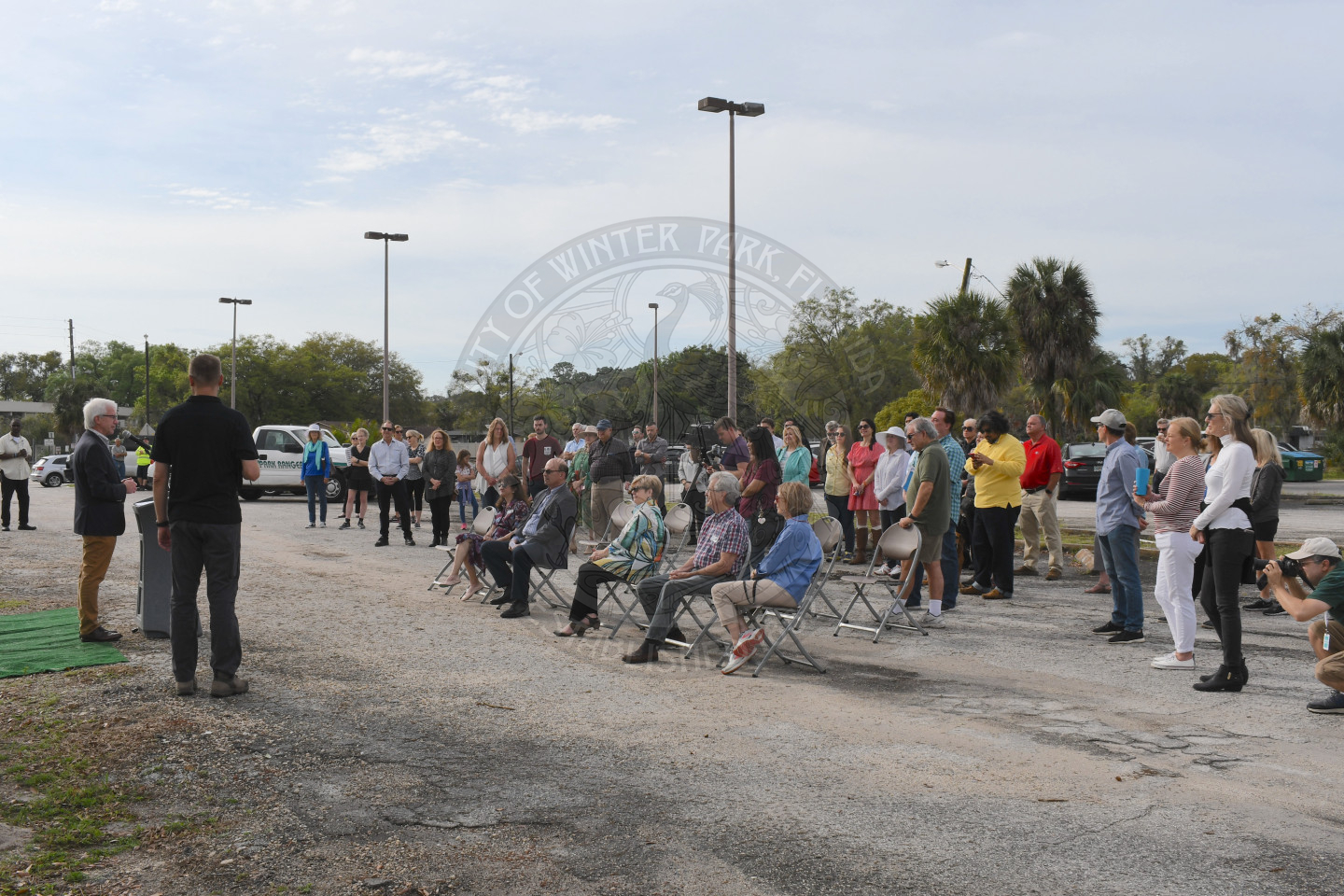 Group of people standing and sitting listening to Mayor Phil Anderson talk