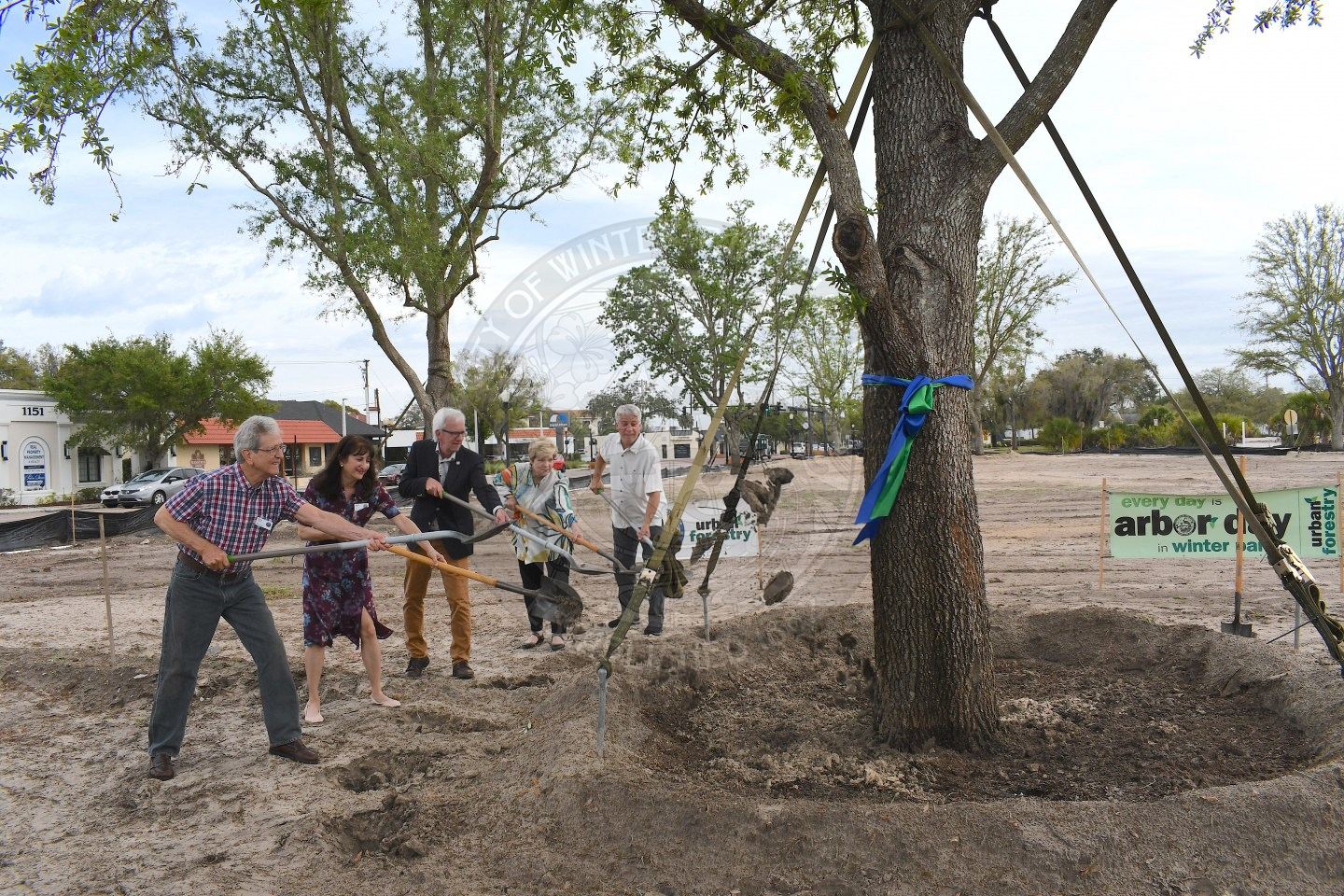 Group of men and women shoveling dirt onto tree to plant it