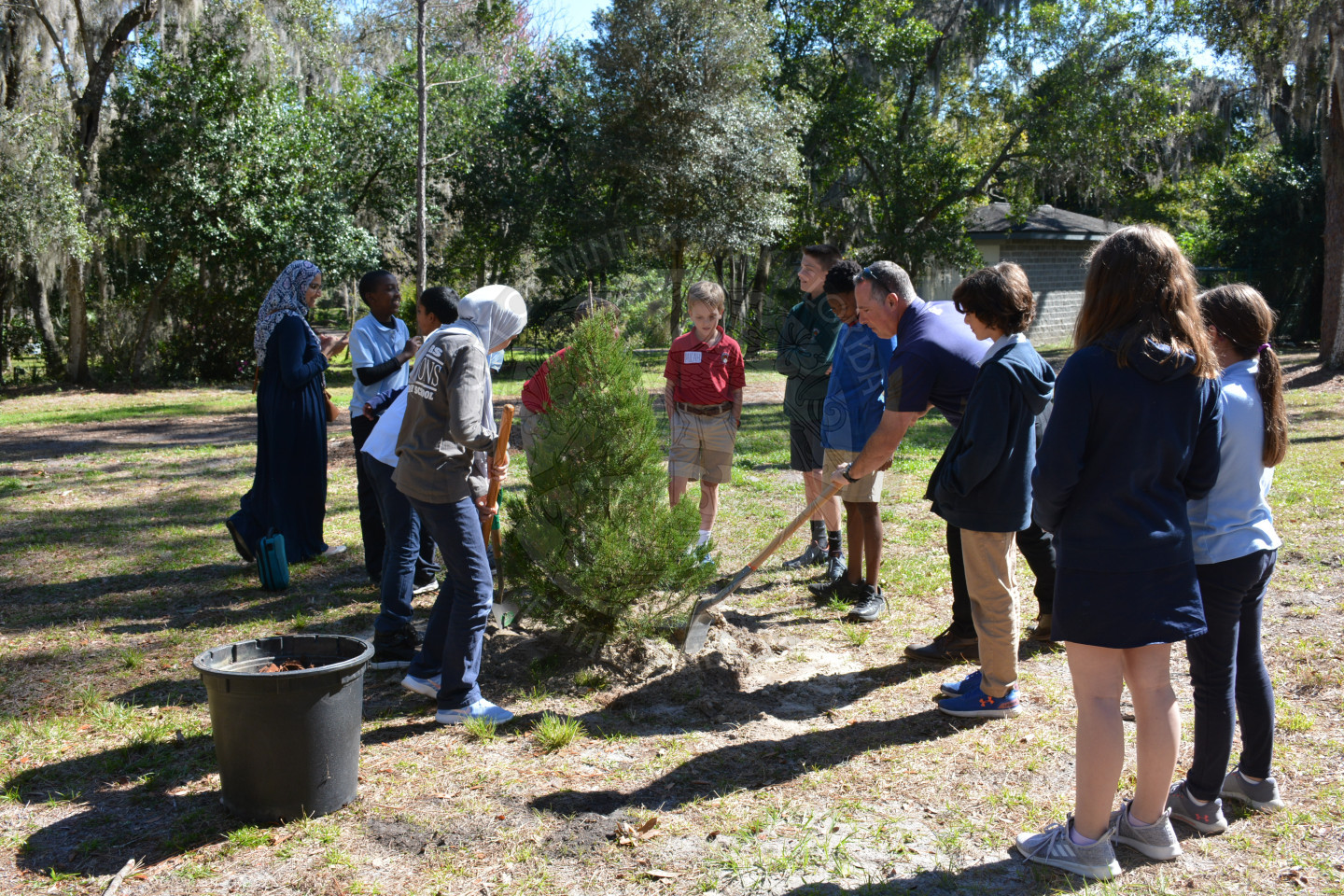Newly planted tree in place and students and teachers adding final dirt to the ground.