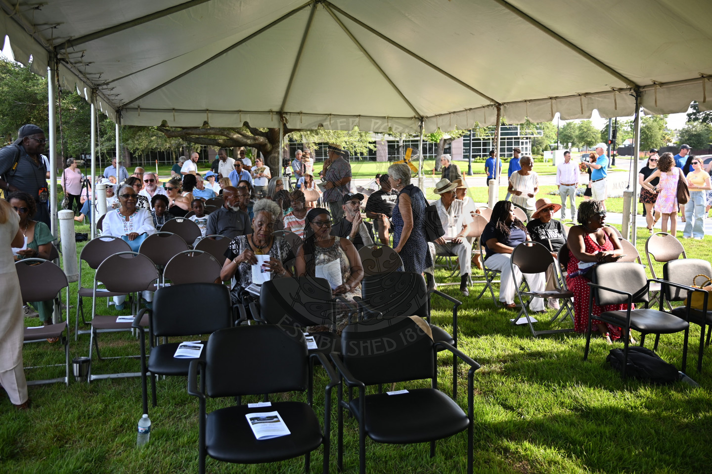 People sitting in chairs underneath a tent waiting for ceremony start.