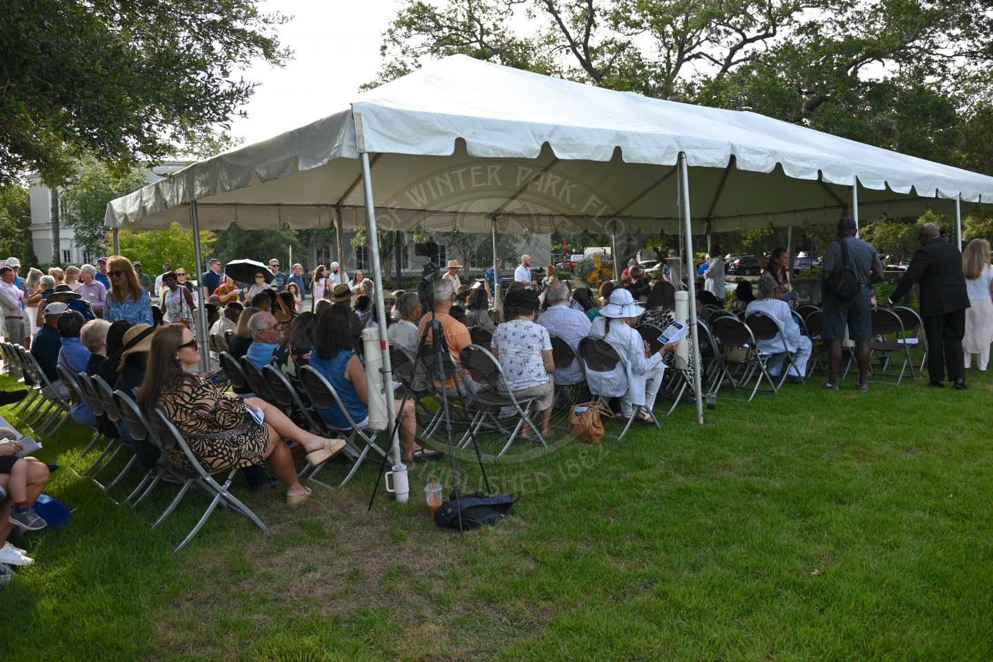 People sitting in chairs underneath a tent waiting for a ceremony start.