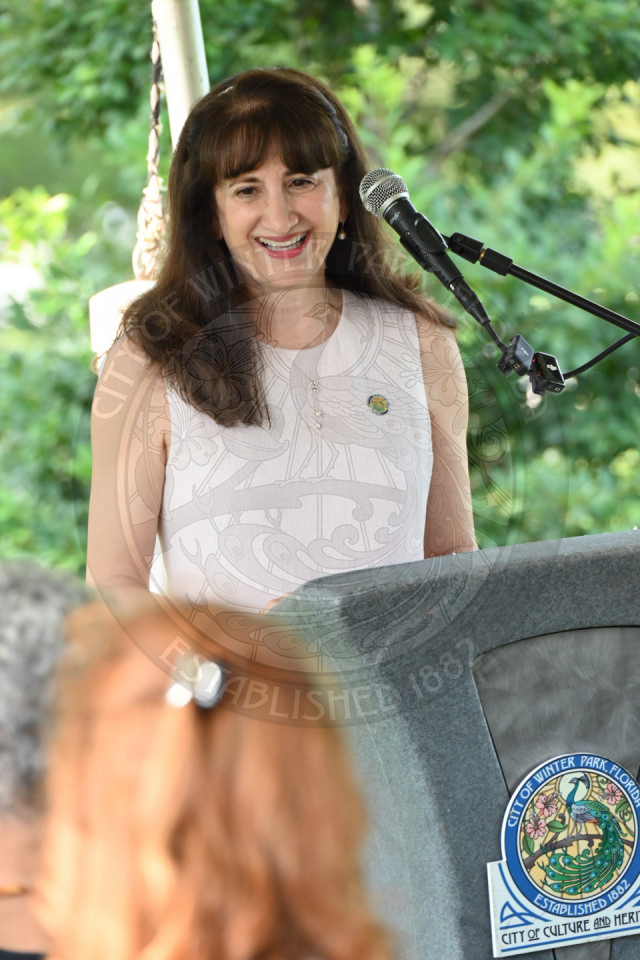 a lady standing behind the podium speaking into a microphone talking and smiling