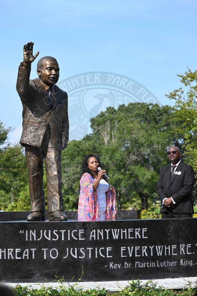 A woman and man standing in front of Martin Luther King, Jr. statue talking into a microphone.