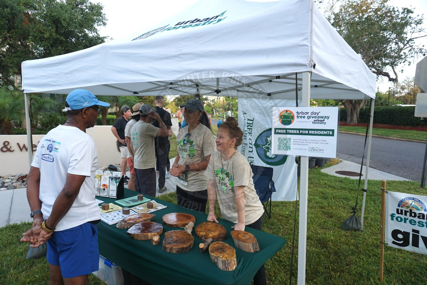 a man talking to the urban forestry division people while they are standing under a white tent.