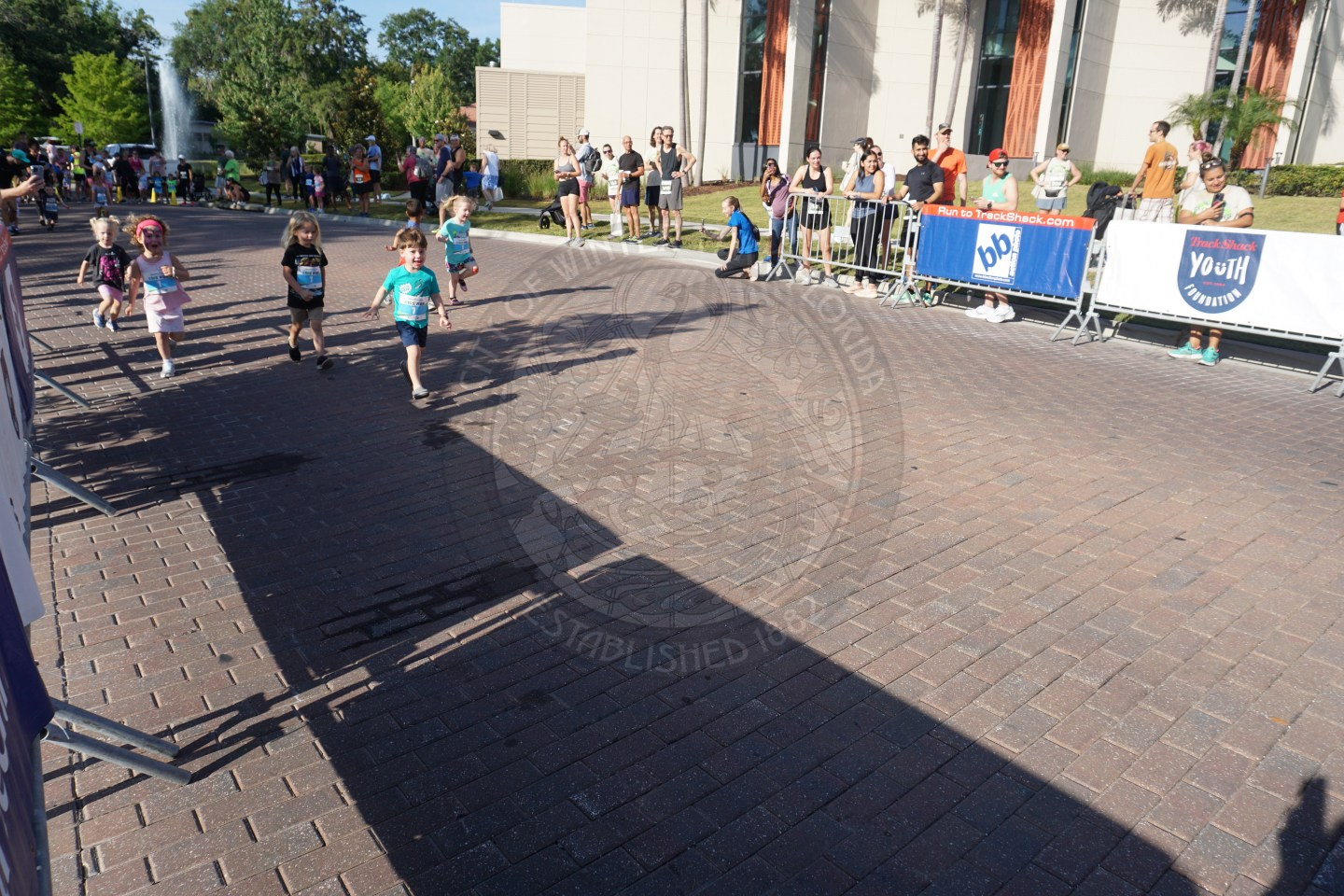 little kids running on the road that is blocked off with race bibs on them. 