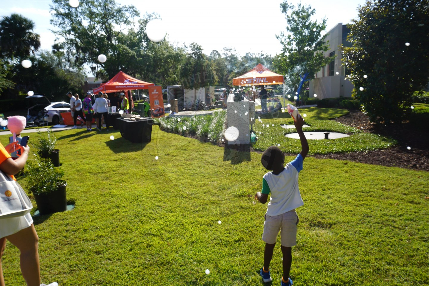 a little boy in a grass area playing with bubbles that are being blown out of a bubble machine