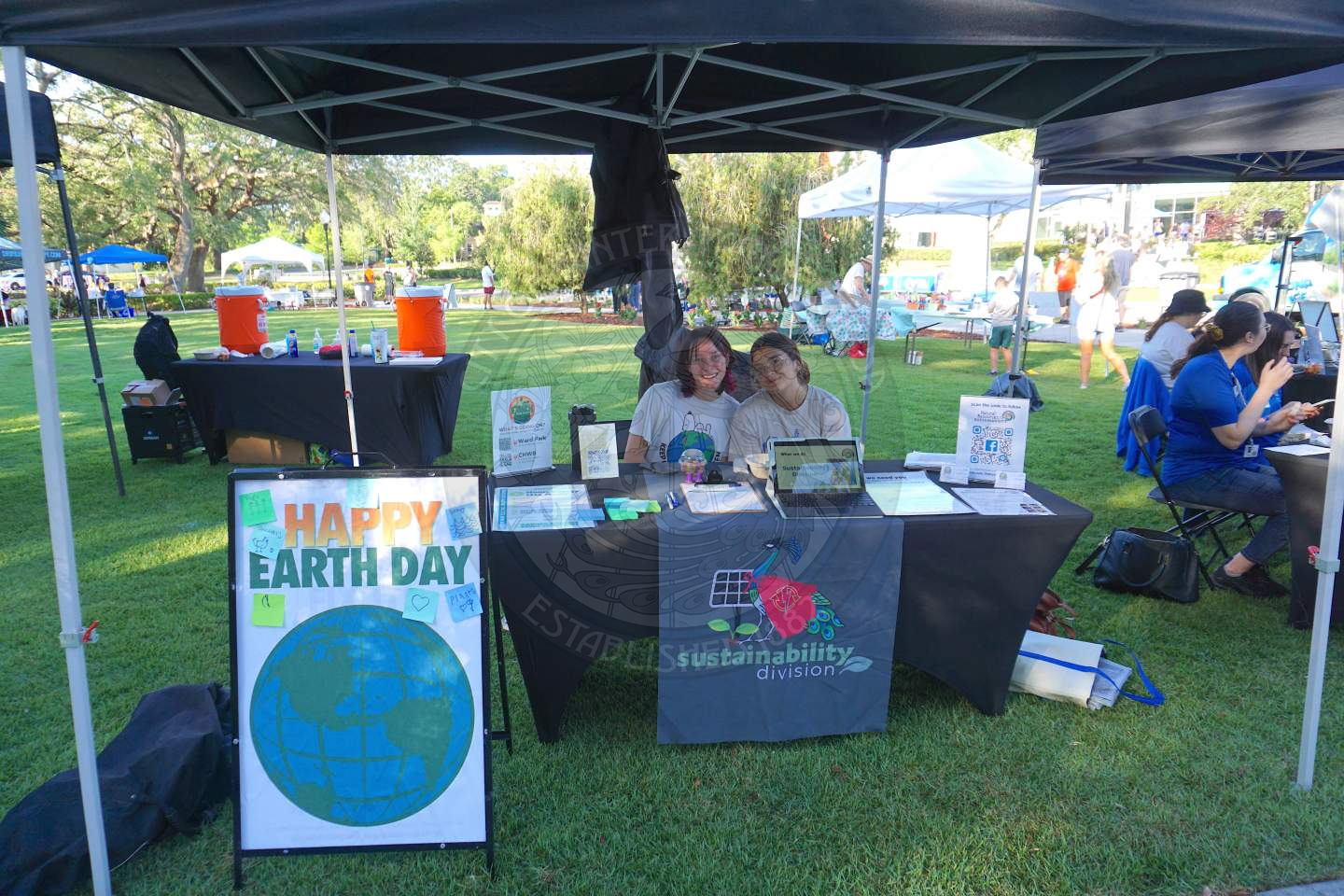 A table with a sustainability divsion labeled tablecloth on it with 2 girl sitting behind the table smiling