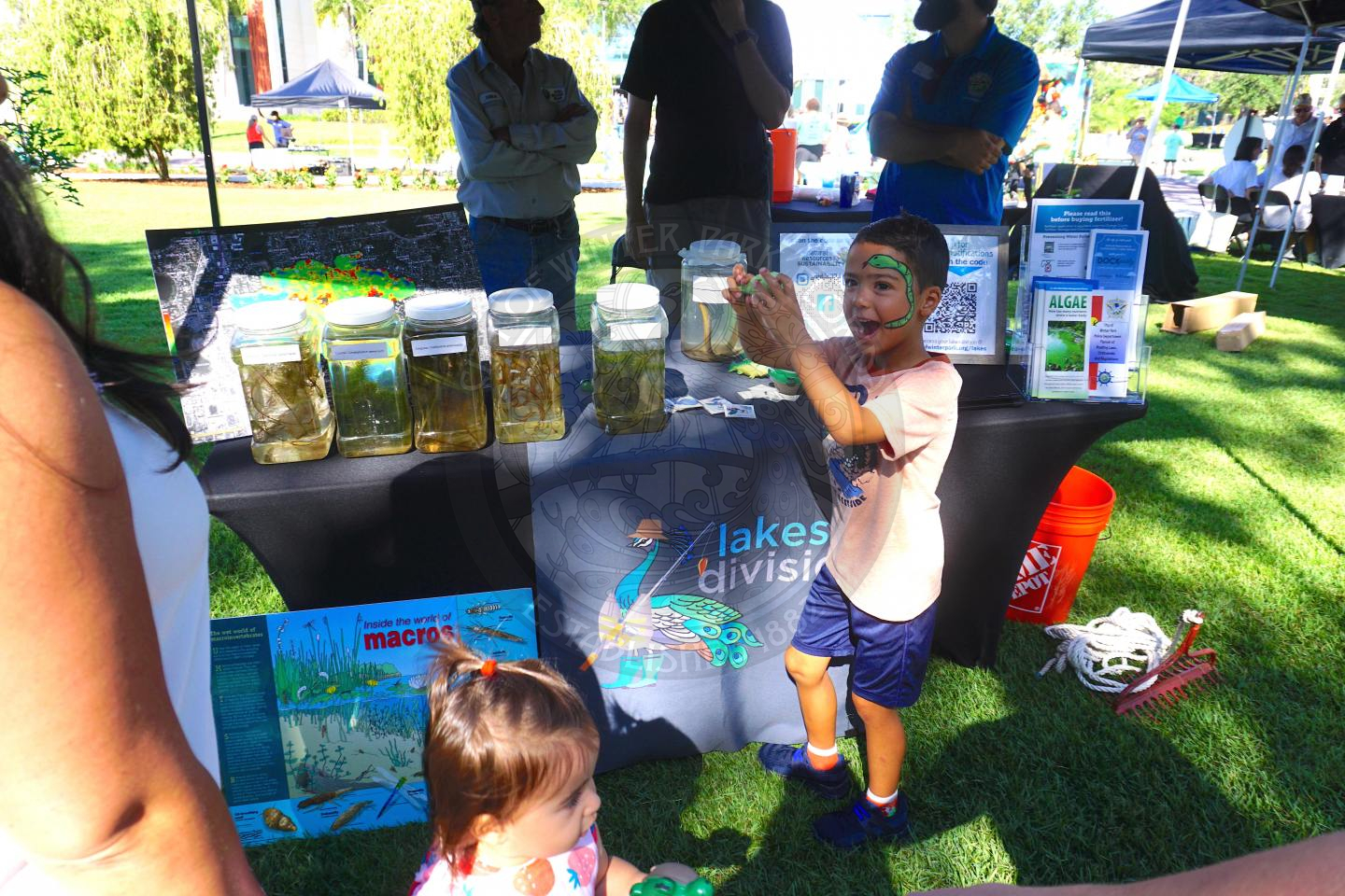 Kid smiling in front of a table that says lakes divison while holding a fish