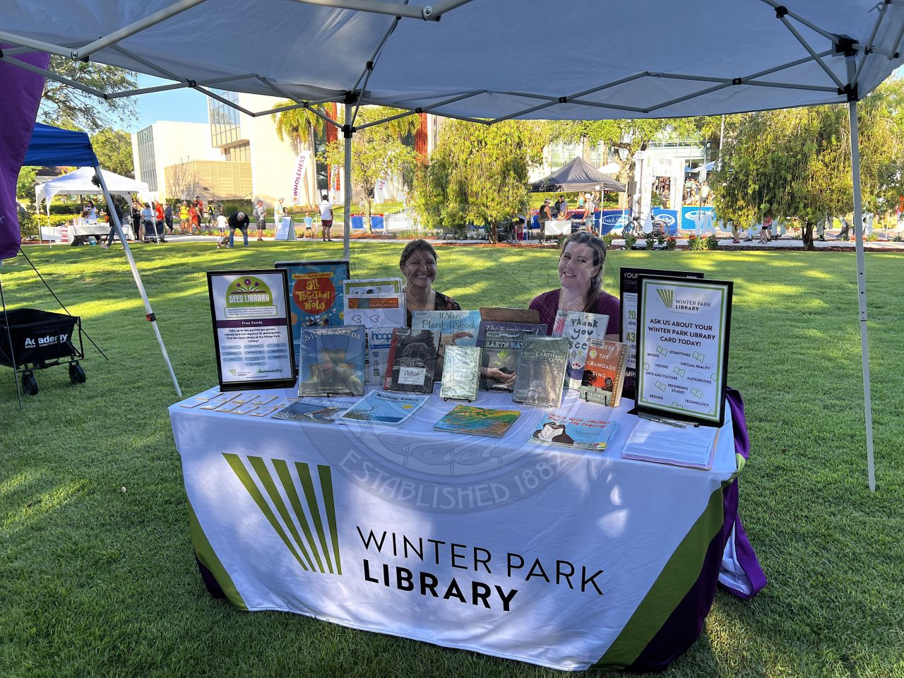 a table filled with information about the Winter Park Library with people sitting behind smiling at the camera