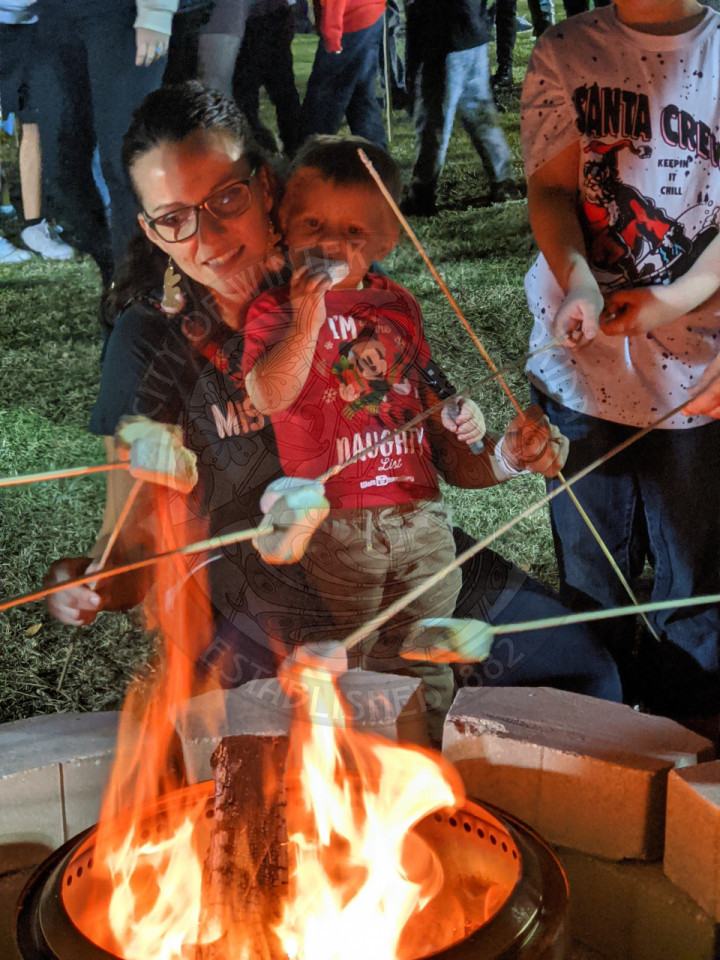 little boy eating a marshmallow while his mom roasts more