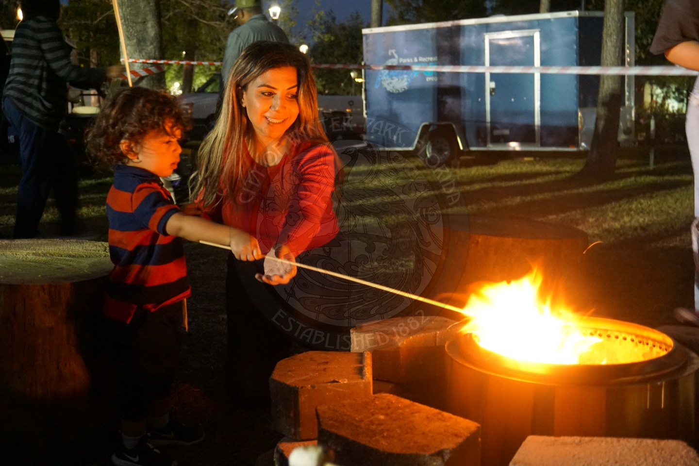a woman and child holding wooden stick in fire pit to toast a marshmellow