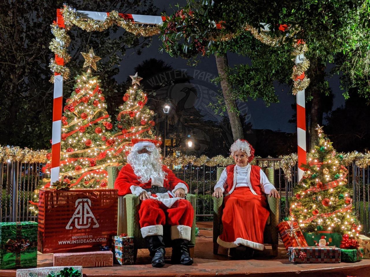 Santa and Mrs. Claus sitting in chairs on a decorated stage