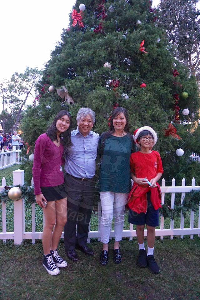 Commissioner Cruzada standing next to his wife, son and daughter in front of a christmas tree that is guarded by a white picket fence.