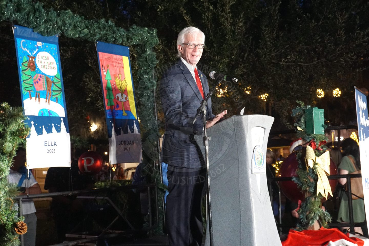 The Mayor of Winter Park standing on a stage behind a podium talking to the crowd standing in front of the stage.