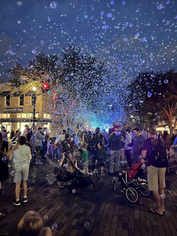 A bunch of people standing on Park Avenue with bubbles blowing in the air and music playing.