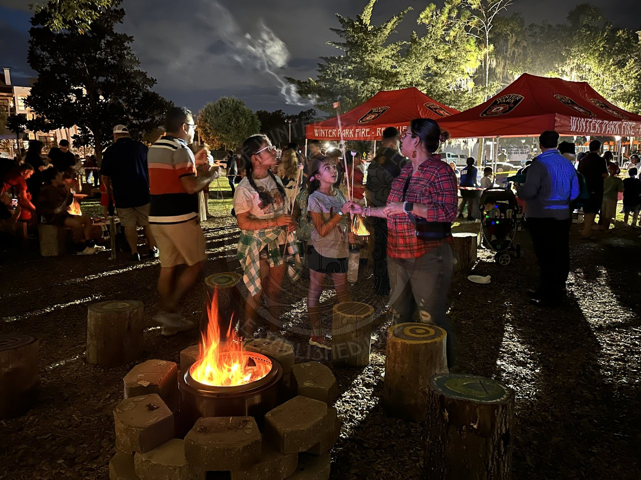 Family standing next a firepit that is surround by cement blocks getting ready to roast marshmallows on a stick.