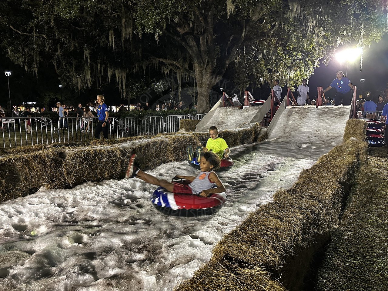a make shift snow slide with 2 kids sitting on pool floats slidding down in the snow while smiling and laughing