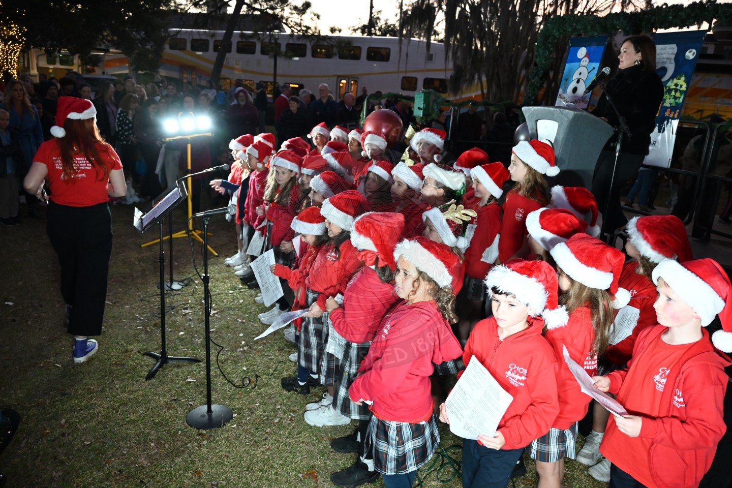 a group of kids wearing santa hats and singing chirstmas carols.