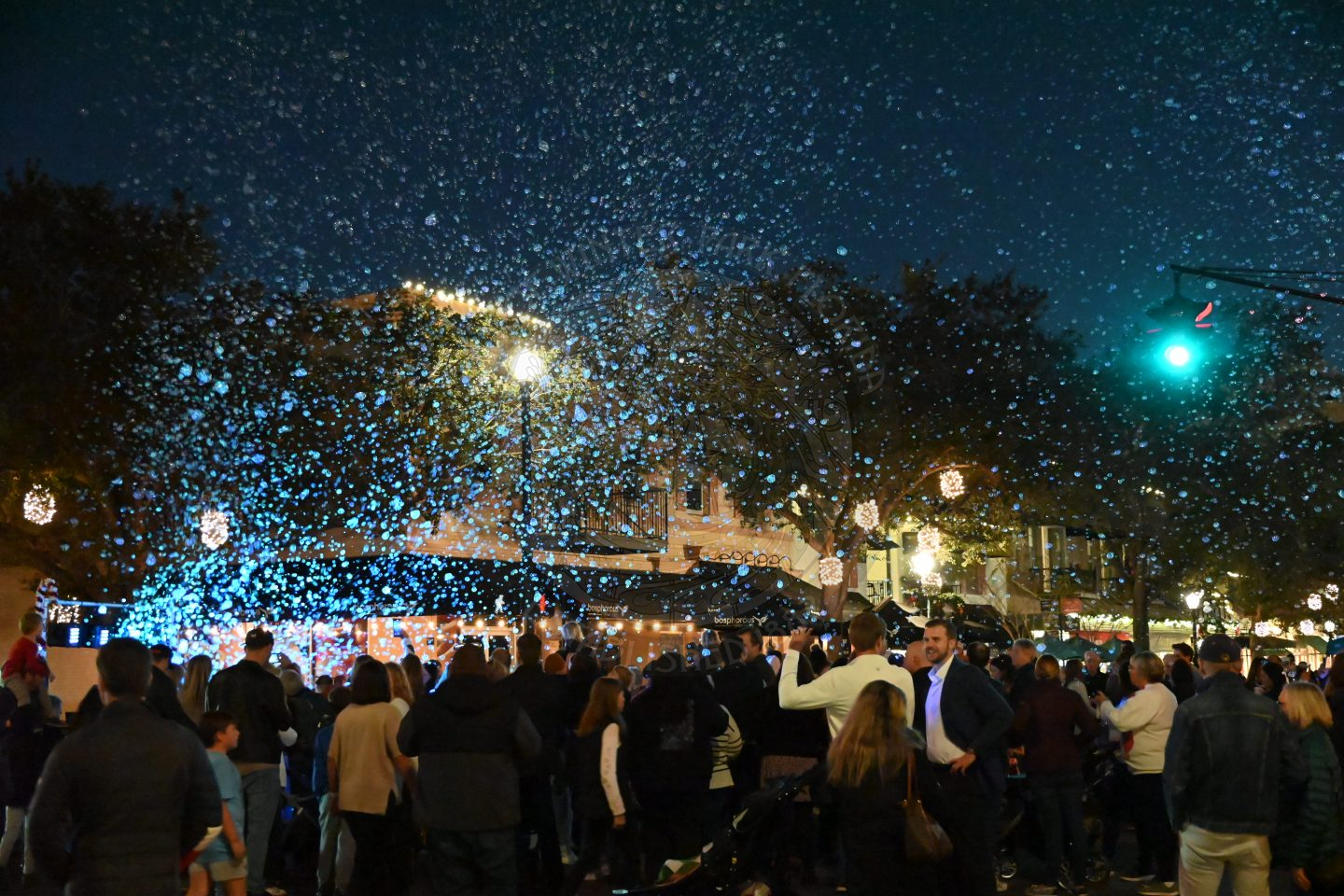 a bubble bus blowing out a bunch of bubbles with people people standing underneath them throwing their hands at them.