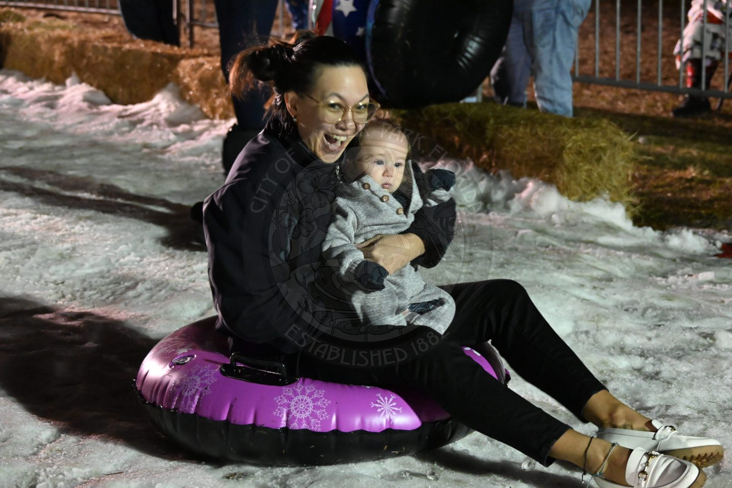 a woman sitting in a pool float while holding her baby and sliding on snow