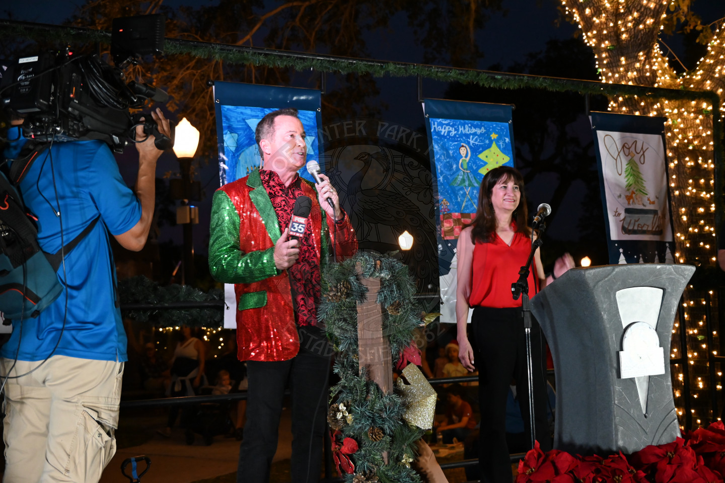 a broadcaster for Fox 35 news talking into a microphone on the stage with the City of Winter Park mayor standing next to him.