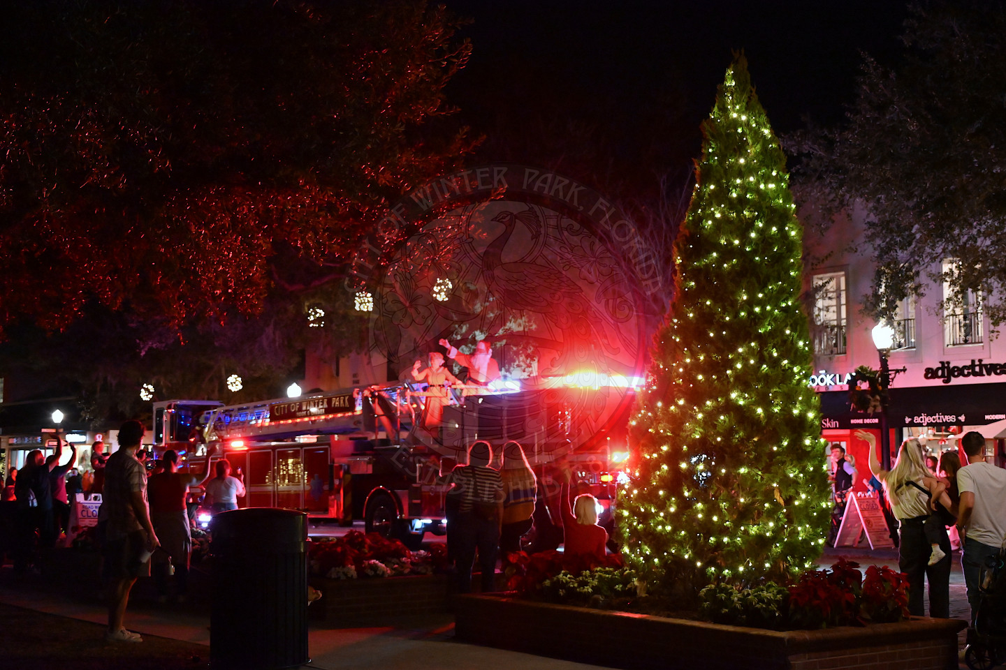 a firetruck lighting up riding down Park Avenue with Mr. and Mrs. Claus on top of the truck waving to the crowd of people overlooking.