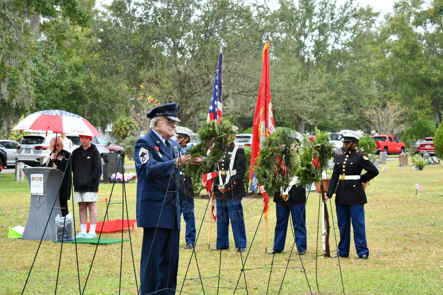 an older man in uniform placing a wreath on an easel.