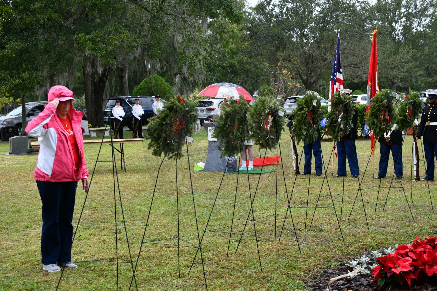 A woman saluting in front of a wreath that she placed on an easel.