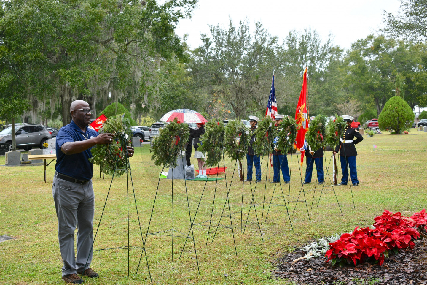 A man hanging up a wreath on easel. There is the color guard behing the easels.
