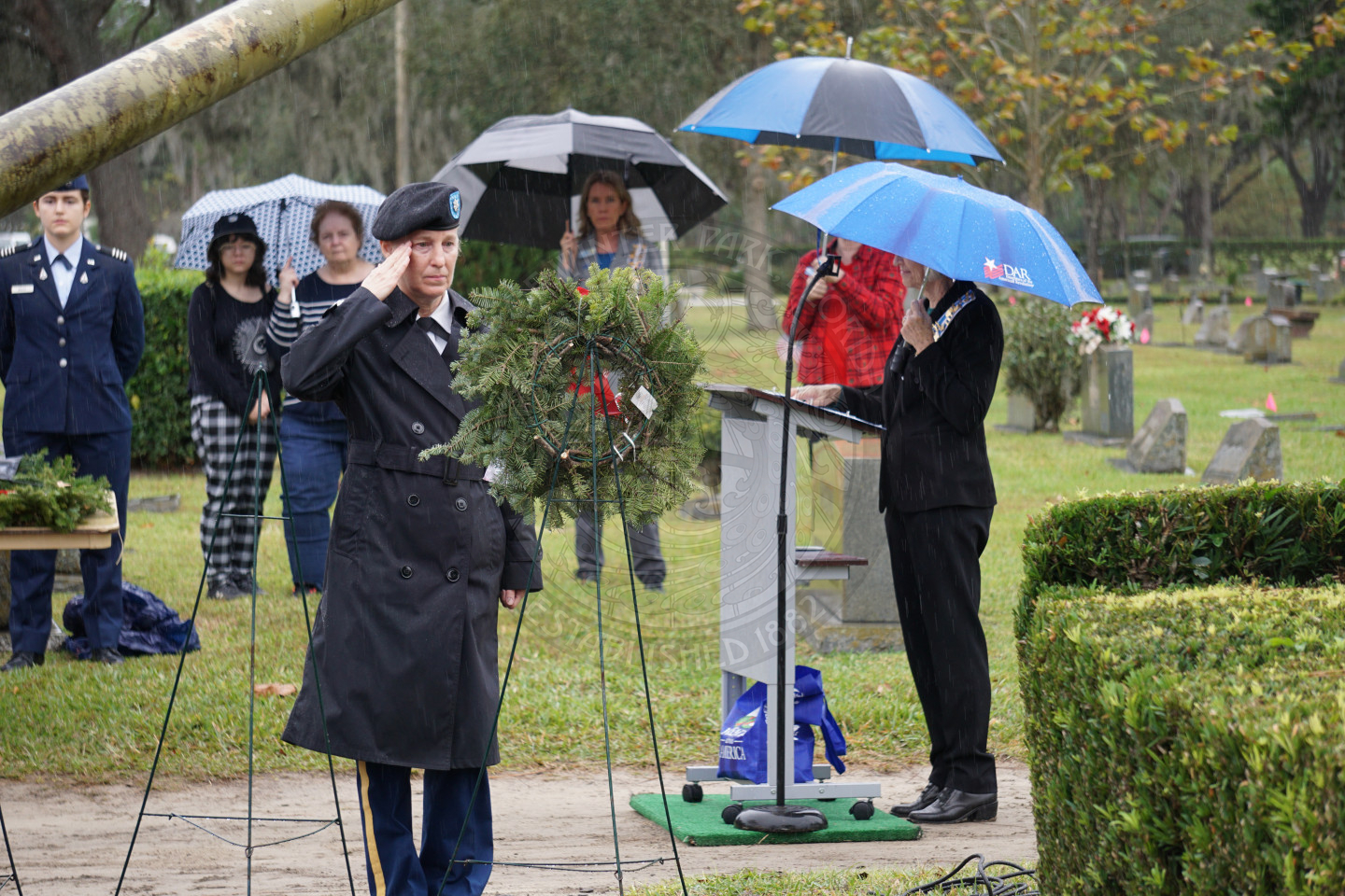 A woman in uniform saluting to the wreath that has been placed on an easle.