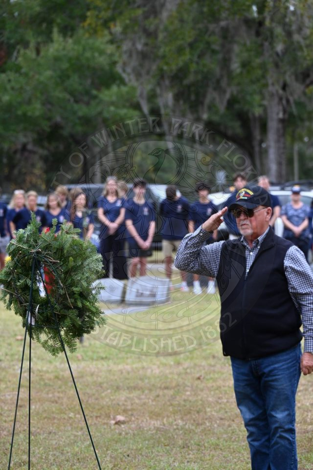 a man saluting to the miltary branch wreath he placed on a stand.