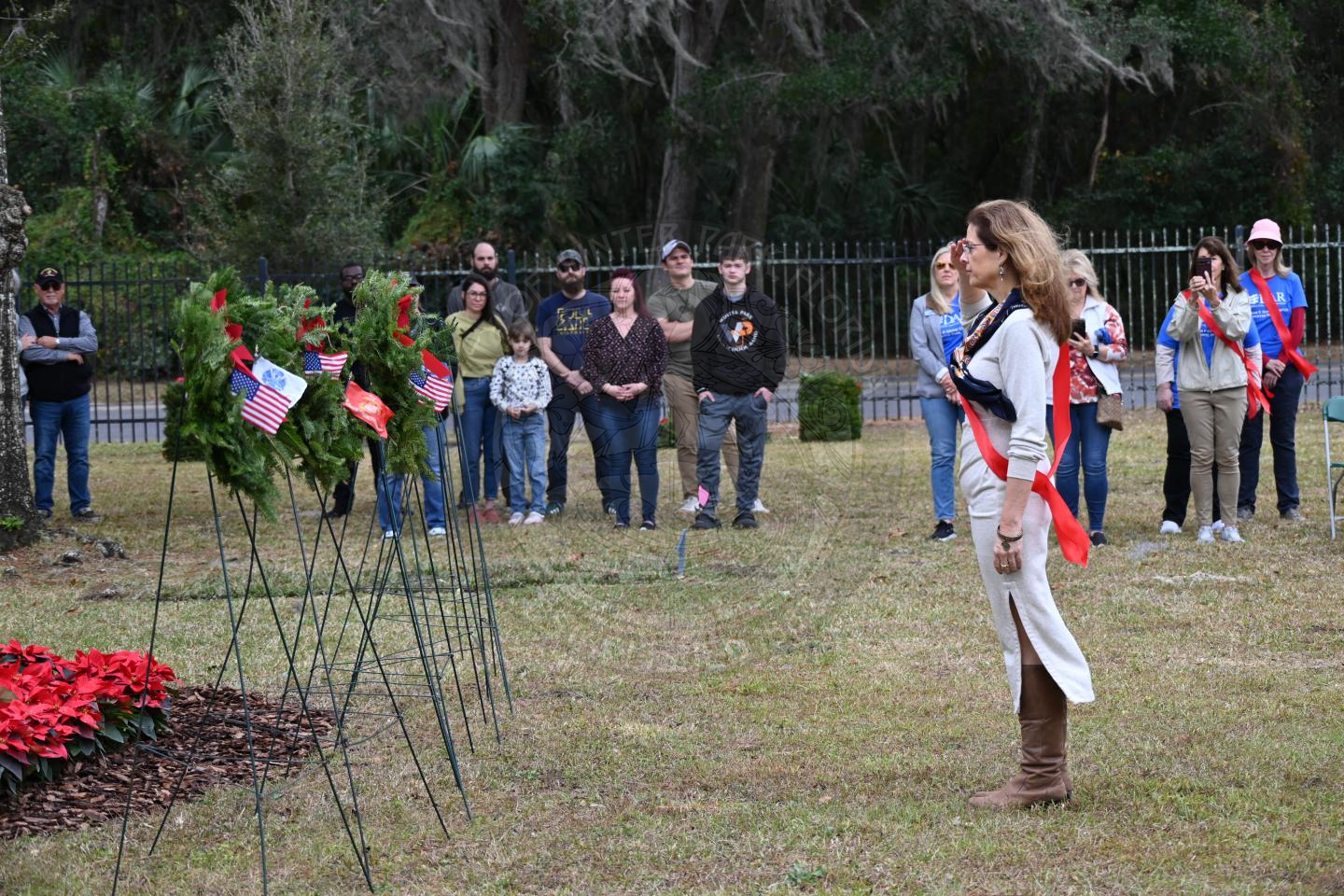 a woman saluting to the miltary branch wreath she placed on a stand.