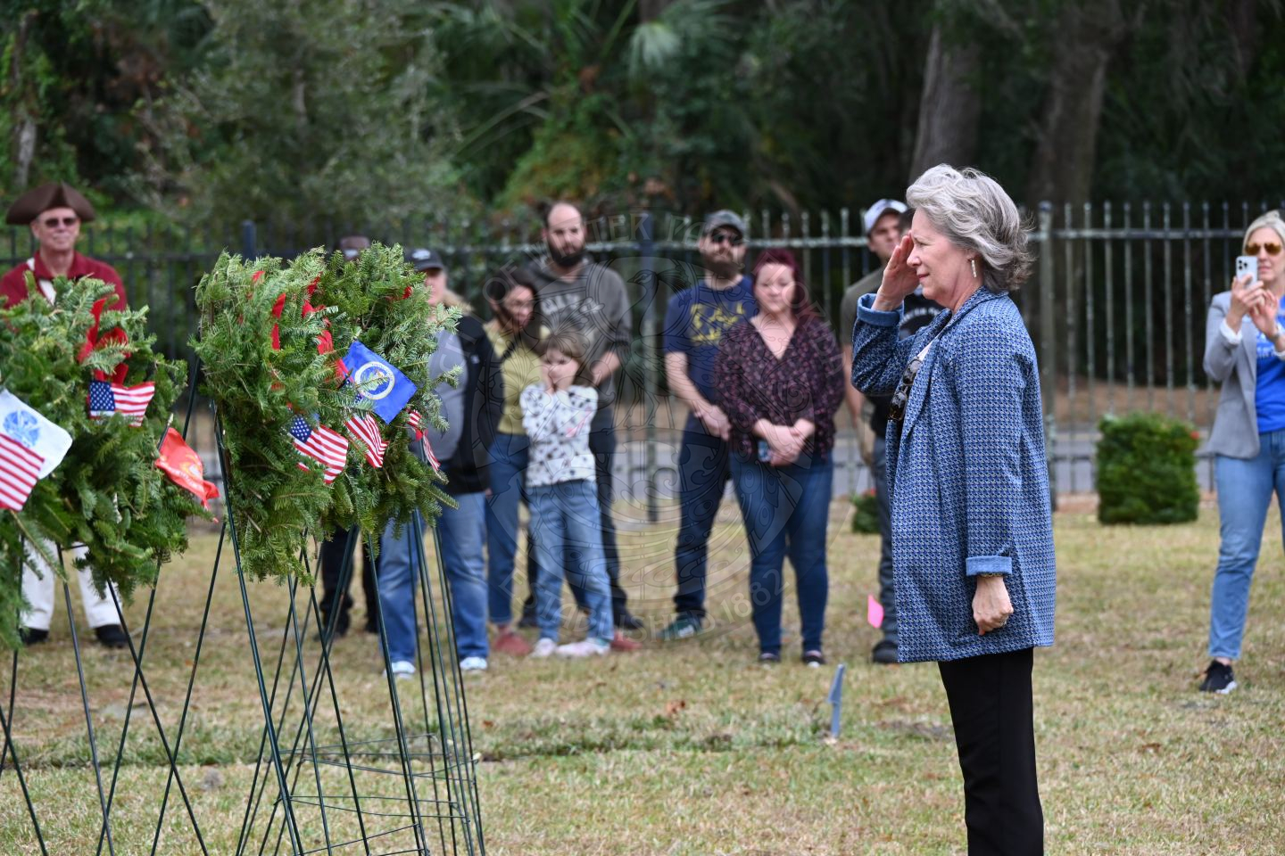 a woman saluting to the miltary branch wreath she placed on a stand.