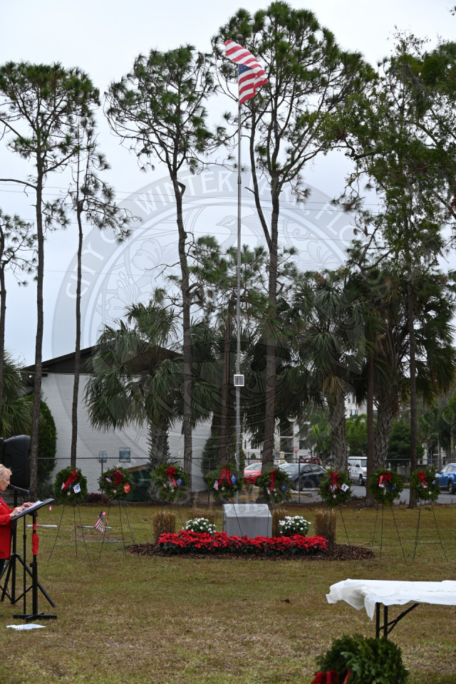 branchs of military wreaths on stand with american flag pole behind it.