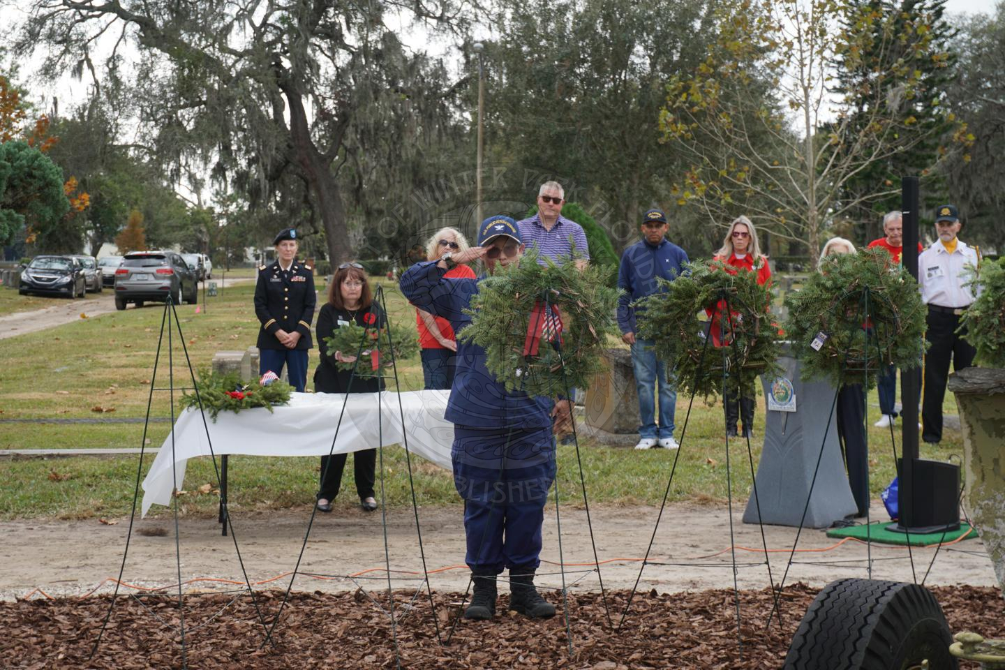 a woman saluting to the miltary branch wreath she placed on a stand.