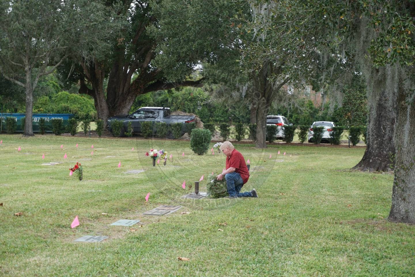 a man on one knee on the grass placing a wreath on a grave.