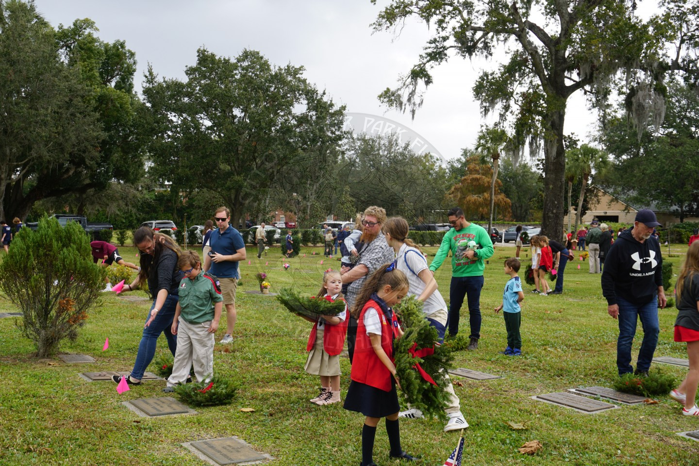 People walking around the cemetary holding wreaths and placing the wreaths on graves. 
