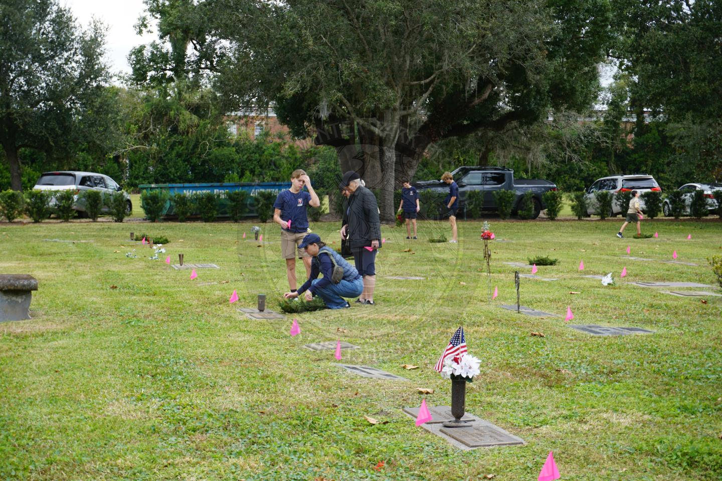 a group of three people standing in front of a grave with a women squatting down placing a wreath on the grave.