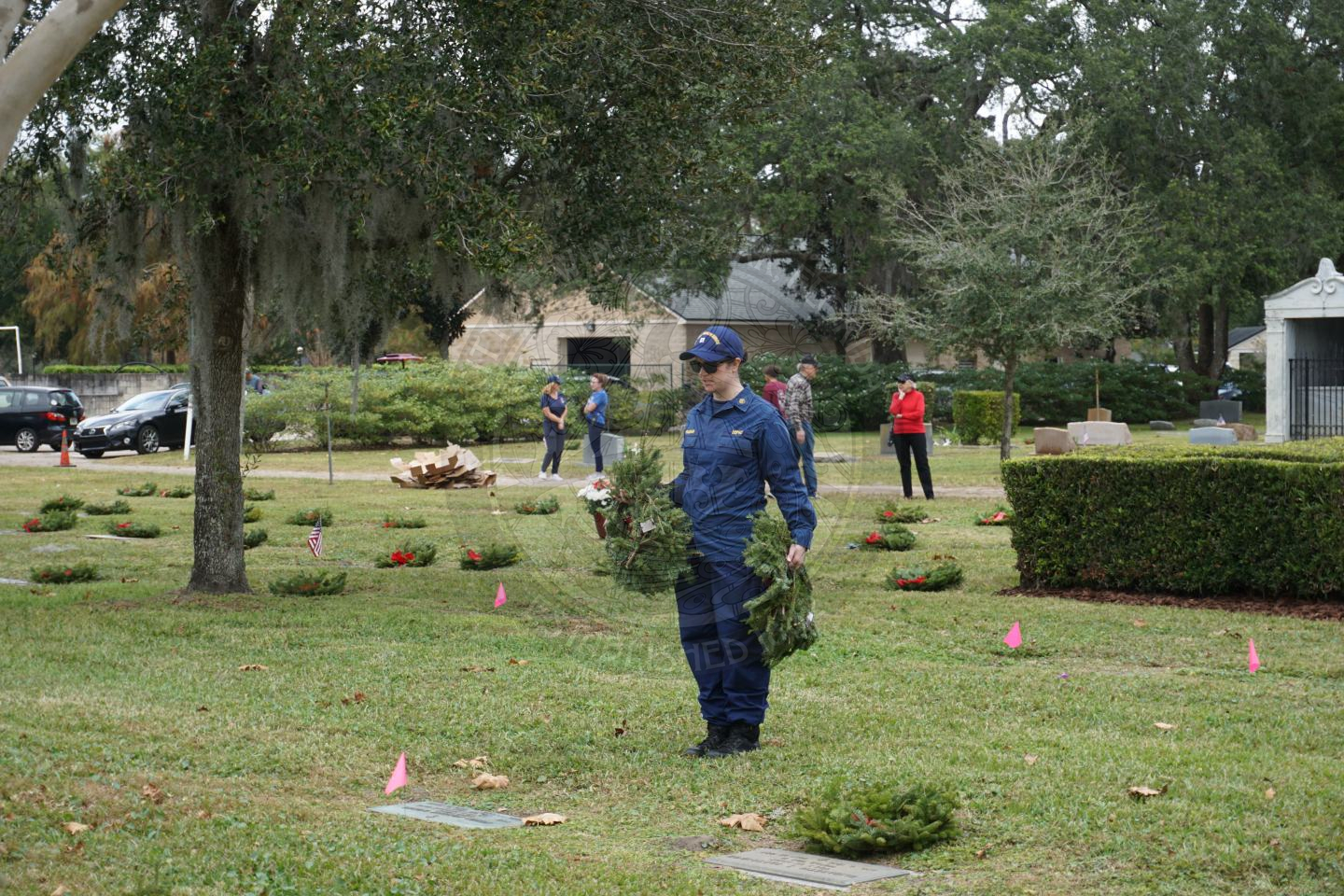 a unifromed woman holding wreaths while talking to the grave about to place the wreath on the grave.