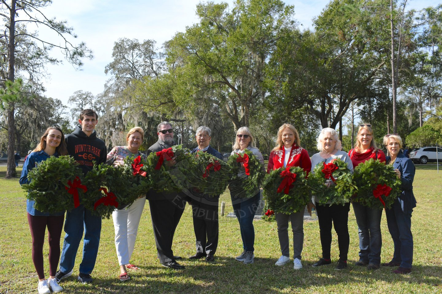 men and women holidng wreaths smiling for a picture at pineywood cemetary