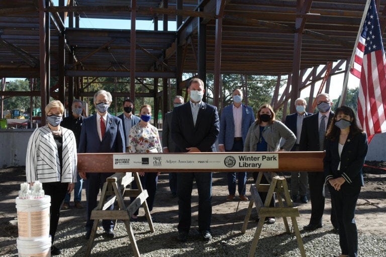Several men and women standing around a steel beam on saw horses