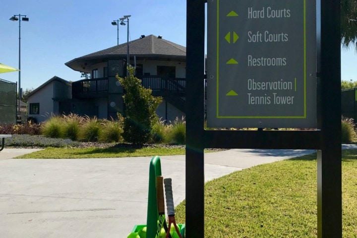 Tennis equipment leaning against Tennis Center Entrance sign with pro shop building in background