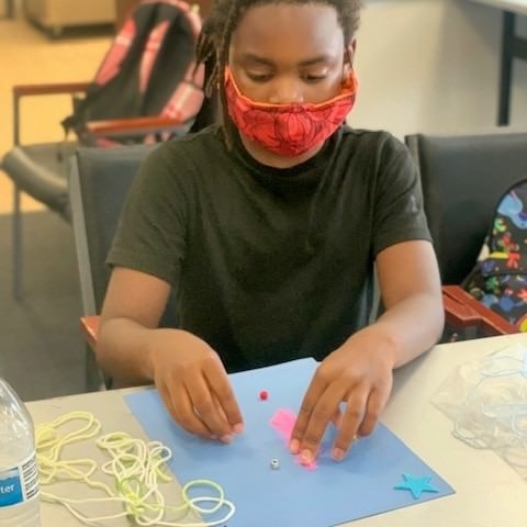 young boy creating art project with paper and string