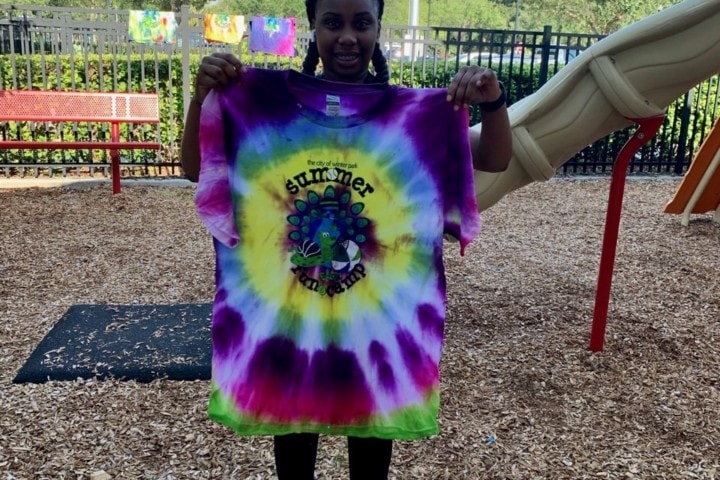 female teen holding up tie-dyed t-shirt in front of herself on playground
