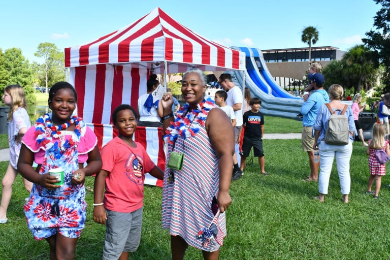 A woman and two kids smiling for the camera standing in front of a red and white striped tent.