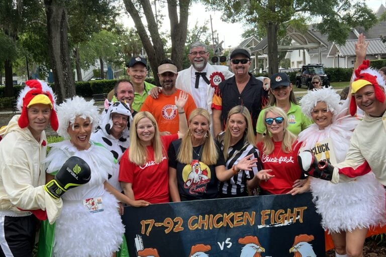a group of people dressed in different chicken companies that are holding a sign that says "17-92 Chicken Fight"